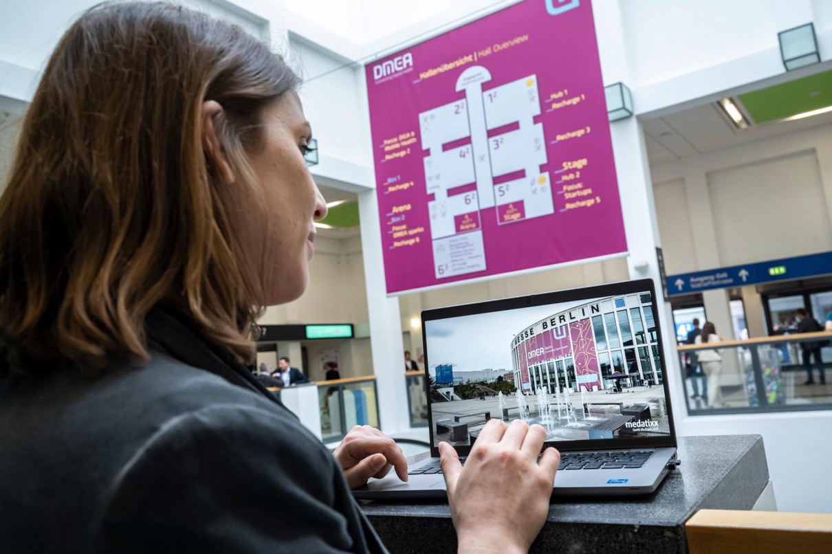 Monitor mit Blick auf ein Online-Plattform Video, dahinter die Messehalle