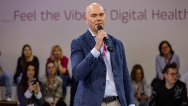 Mann im Anzug auf einer der DMEA-Bühnen, Publikum im Hintergrund – der Schriftzug „Feel the Vibe of Digital Health“ an der Wand 
