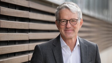 Portrait von Matthias Meierhofer im Anzug vor einer Wand mit Holzbalken 