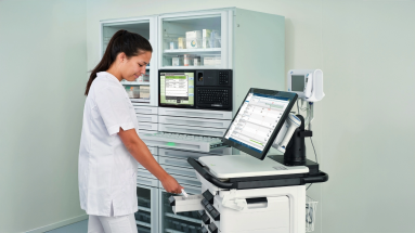 A nurse stands at a smart AMiS ward trolley and a digital medication cabinet.